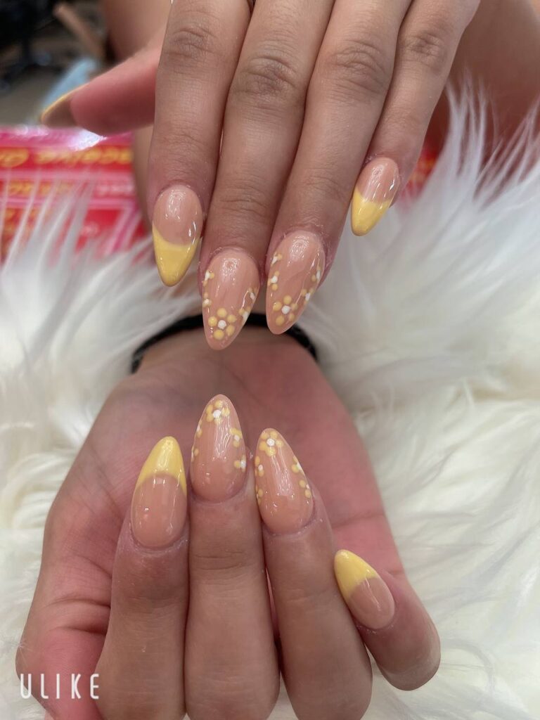 Sunny yellow almond-shaped nails with delicate white polka dot art, created by the talented team at The Grand Nails of America in Houston
