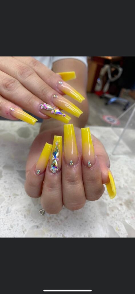 Striking sunny yellow nail design with dazzling rhinestone embellishments, presented by The Grand Nails of America in Houston.