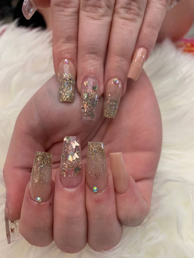 Chic coffin-shaped nails with a glittering gold finish and subtle gemstone embellishments, a signature style at The Grand Nails of America in Houston.